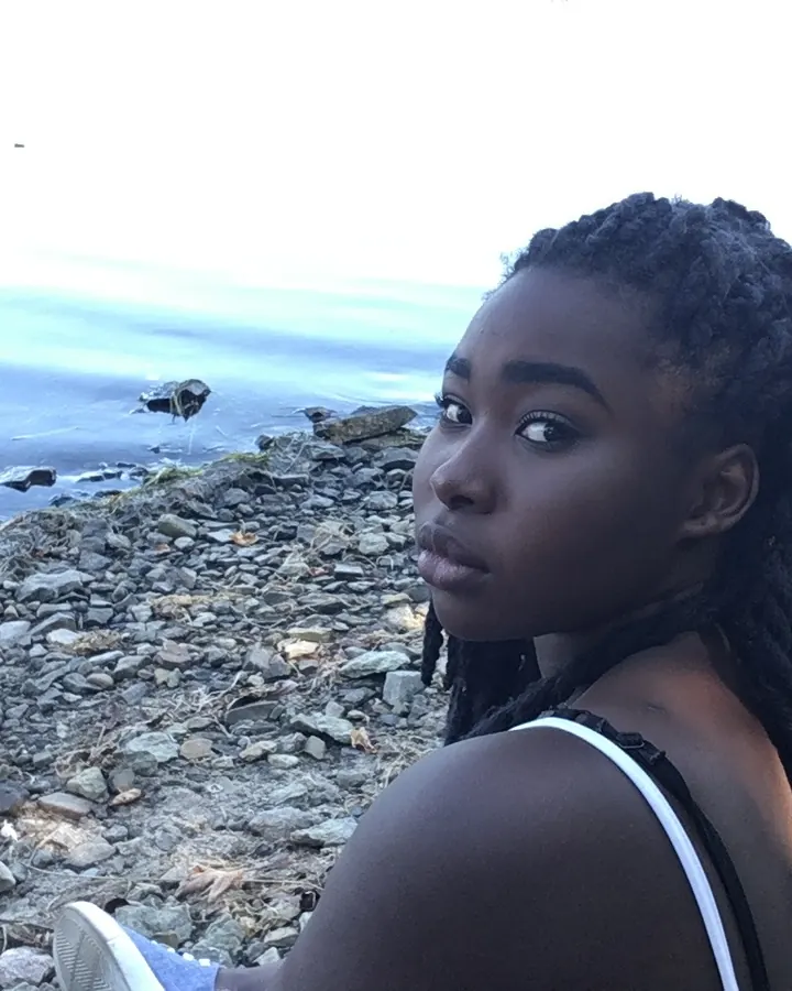 Femme aux cheveux bruns, portant un haut noir, assise, regardant l'appareil