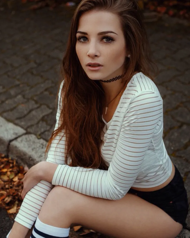 Femme aux cheveux bruns, en haut rayé blanc et noir, genoux croisés, regardant l'appareil, collant noir, chaussettes blanches rayées.