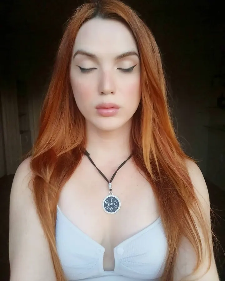 Femme aux cheveux roux, vêtue d’un haut blanc, portant un pendentif, regardant vers le bas