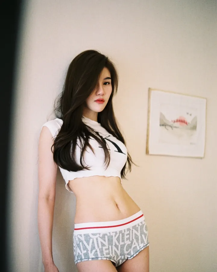 Femme asiatique aux cheveux foncés, regard direct, tenue décontractée, pose naturelle contre un mur clair