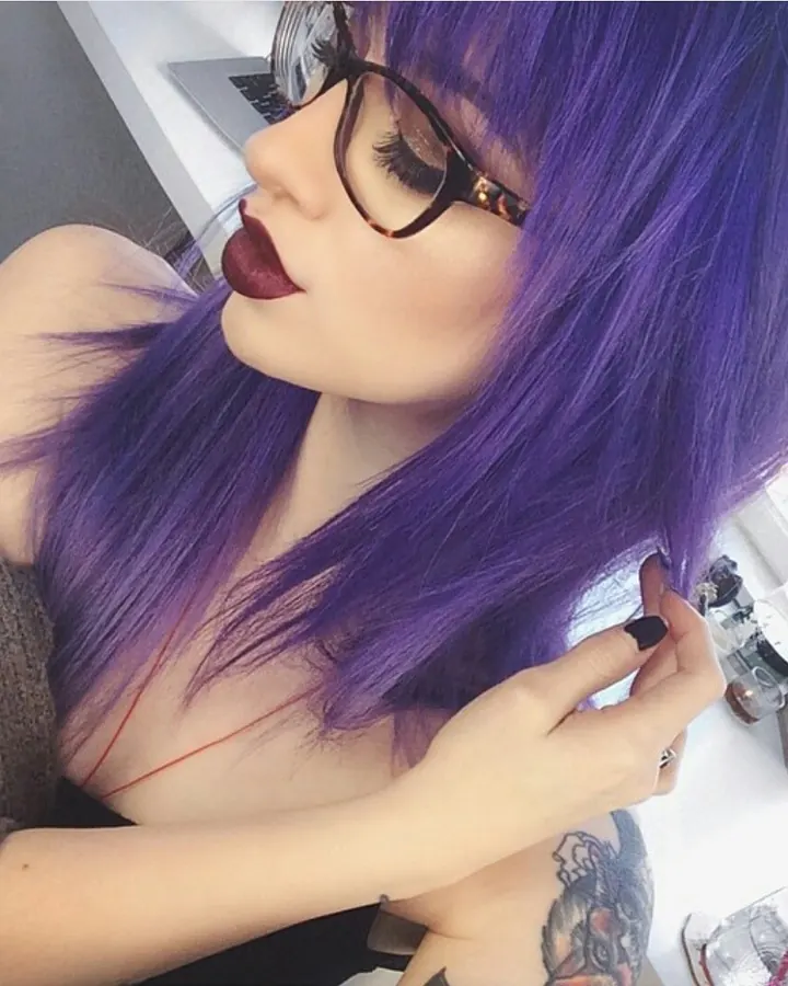 Femme aux cheveux roux, vêtue d'un haut gris, debout dans la neige, les mains dans les cheveux, regardant vers l'avant.