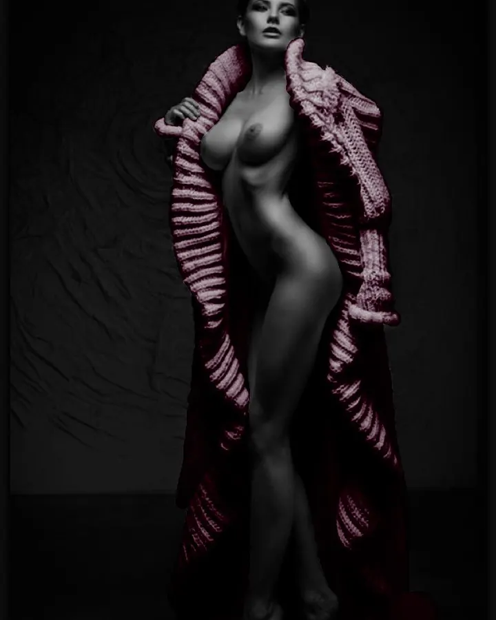 Femme nue, allongée sur un lit blanc, mains près du visage, regard sensuel, bracelet doré au poignet.
