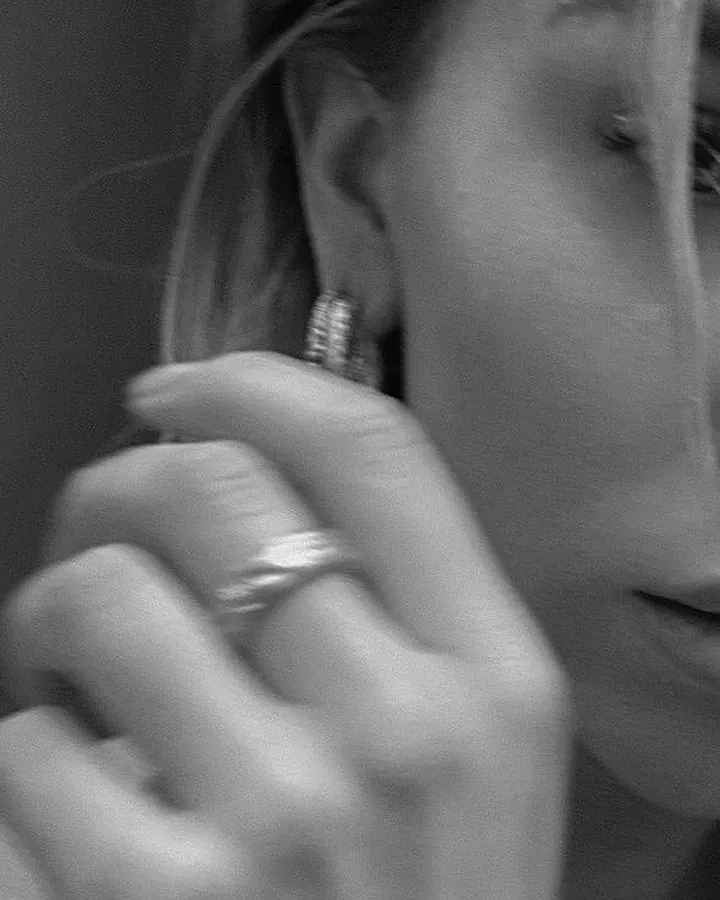 Plan rapproché d'une femme en noir et blanc, main près de l'oreille, portant une bague et un bijou d'oreille.