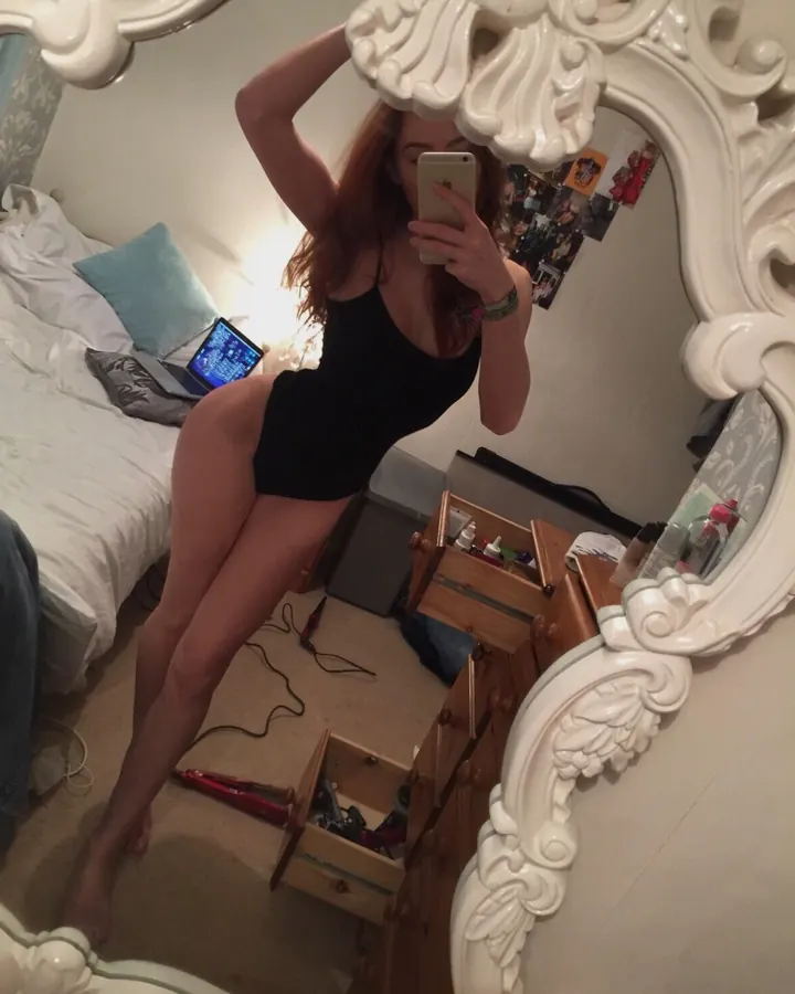 Femme aux cheveux roux, portant un haut noir, prenant un selfie dans un miroir baroque, dans une chambre.