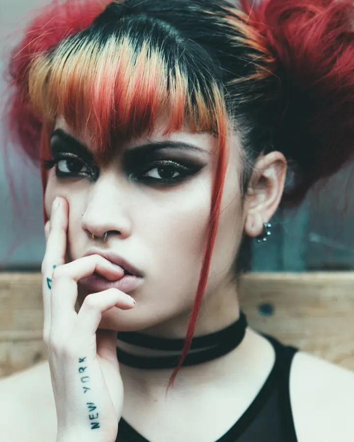 Femme aux cheveux roux, vêtue d'un haut noir, tenant sa main près de son visage, tatouage visible sur le bras.