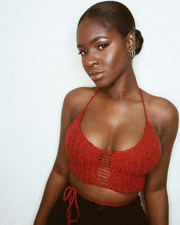 Femme aux cheveux noirs, peau mate, portant un haut rouge à lacets, regardant directement l'objectif avec assurance.