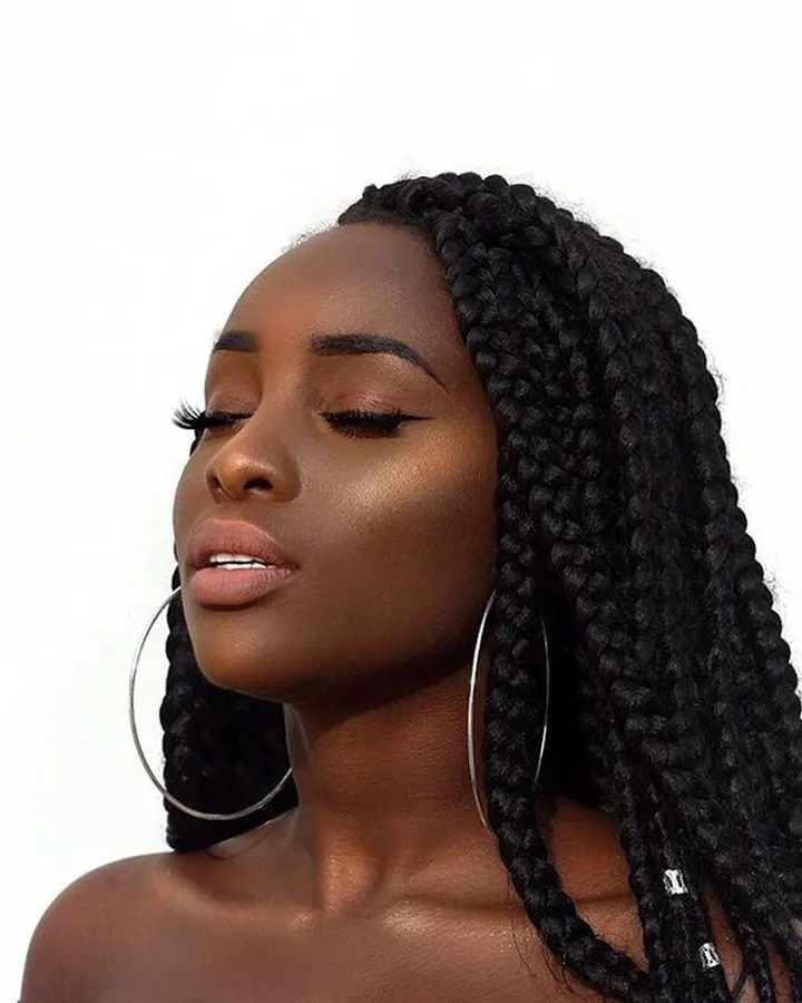 Femme aux cheveux noirs, peau mate, boucles d'oreilles fines, regard fermé, profil de côté, lumière douce.