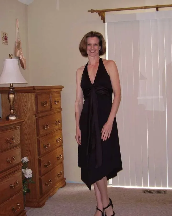 Femme aux cheveux bruns, portant un haut noir et un short assorti, tenant un verre rose.