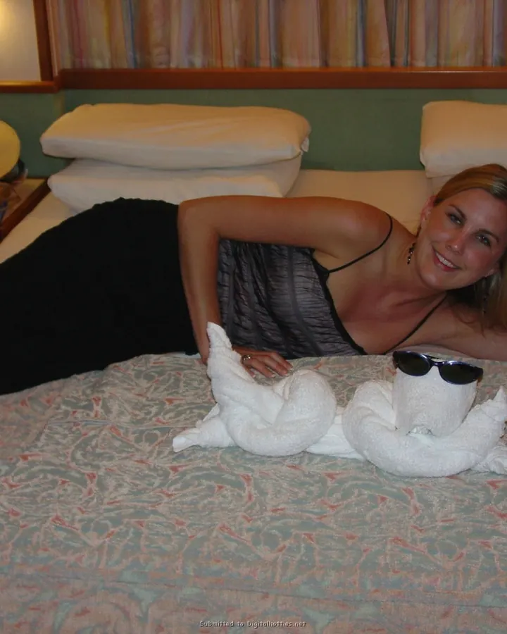 Femme blonde allongée sur un lit, souriante, avec des serviettes en forme d'oiseaux devant elle.