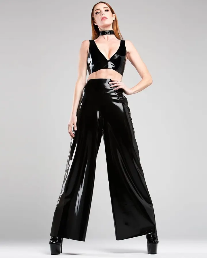 Femme aux cheveux roux, en tenue de latex noir, posant de face sur un fond gris neutre