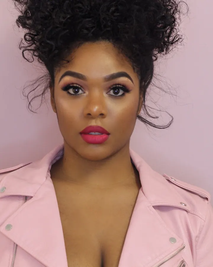 Femme afro-américaine aux cheveux noirs, en tenue de cuir noir, posant de profil sur un fond gris neutre